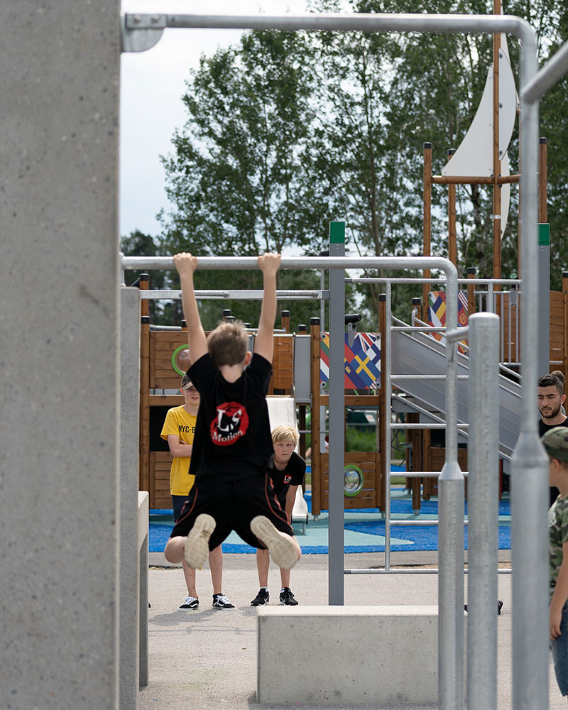 A  young boy is hanging off exercise bars at a parkour park.